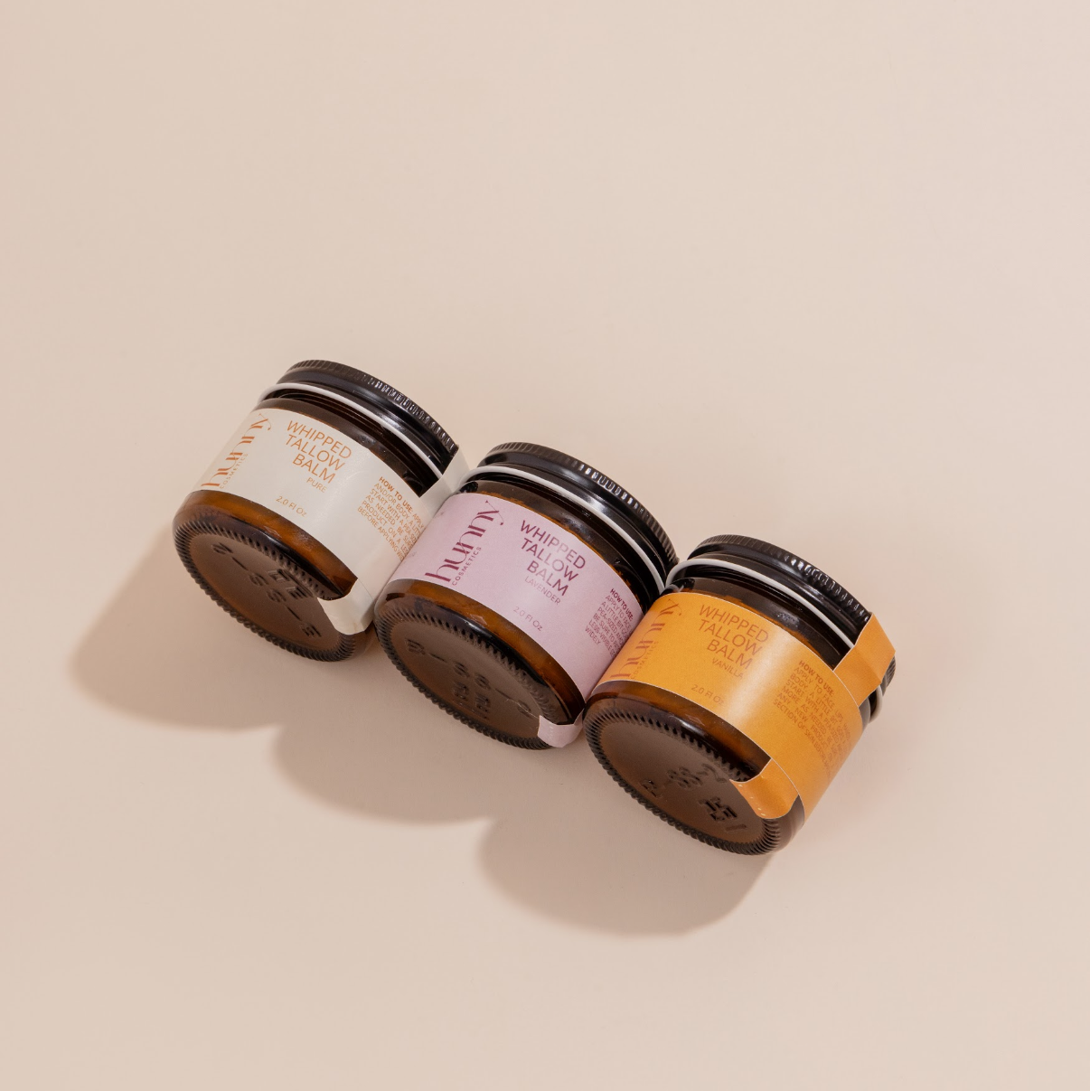 Three jars of 'Whipped Tallow Balm' on a beige background.